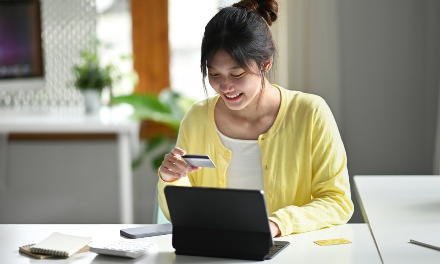 Young woman sitting in front of a tablet and holding a credit card ready to make an online purchase.