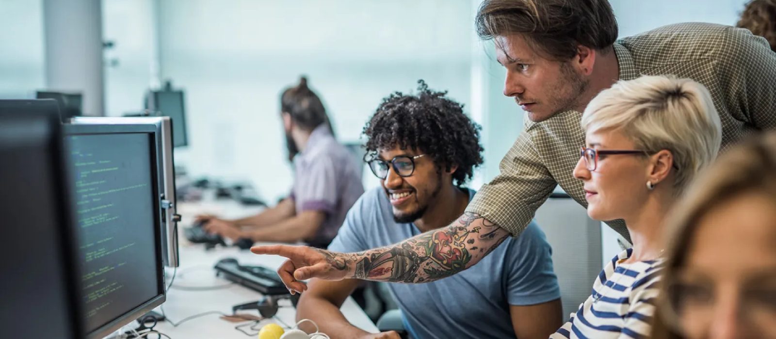 Group of three engineers - two men and a woman - collaborating around a workspace reviewing code displayed on a screen.