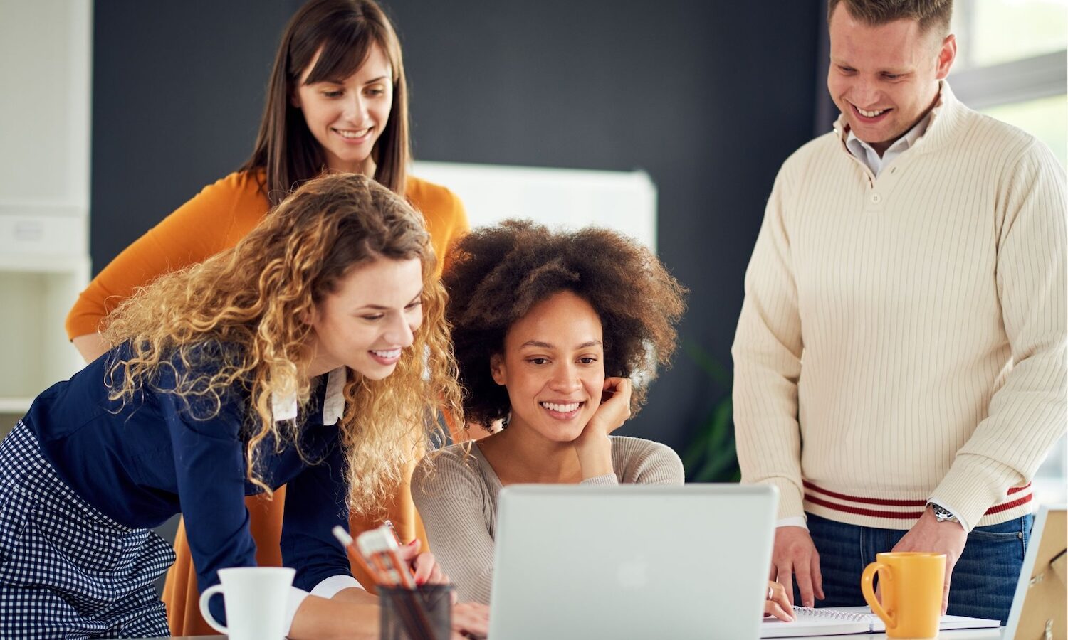 Colleagues gathered around a laptop smiling.