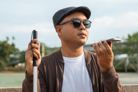 Young asian blind man using a cell phone. Accessibility fundamentals like ARIA labels and alt text help people with visual disabilities navigate the web.